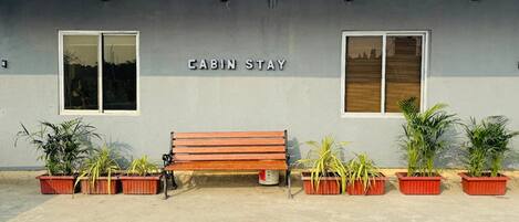 A building labeled 'CABIN STAY' with a wooden bench and potted plants in front.