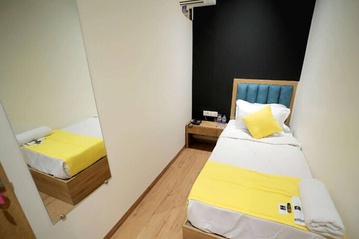 A small hotel room with two beds, a mirror, a nightstand, and a wall-mounted air conditioner.