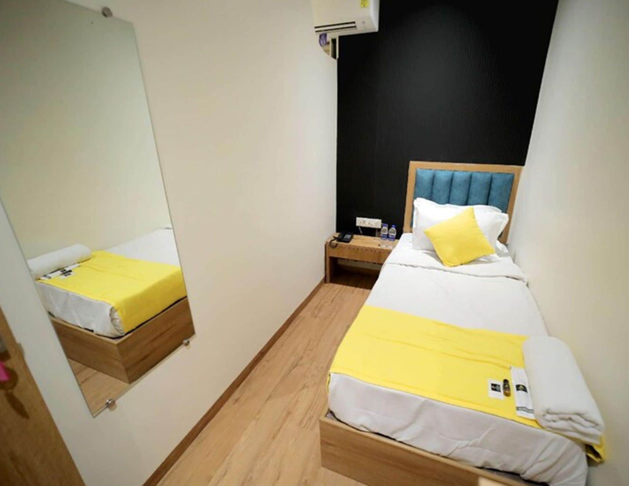 Ein kleines Hotelzimmer mit zwei Betten, einem Spiegel, einem Nachttisch und einer Wand-Klimaanlage.
