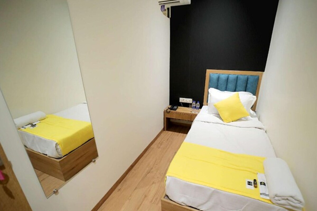 A small hotel room with two beds, a mirror, a nightstand, and a wall-mounted air conditioner.