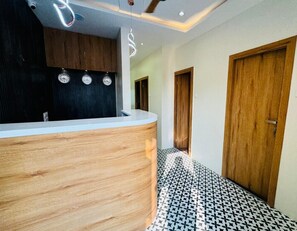 A reception area with a wooden counter, a black wall with clocks, and a patterned floor. - Cabinstay Airport (Mumbai)
