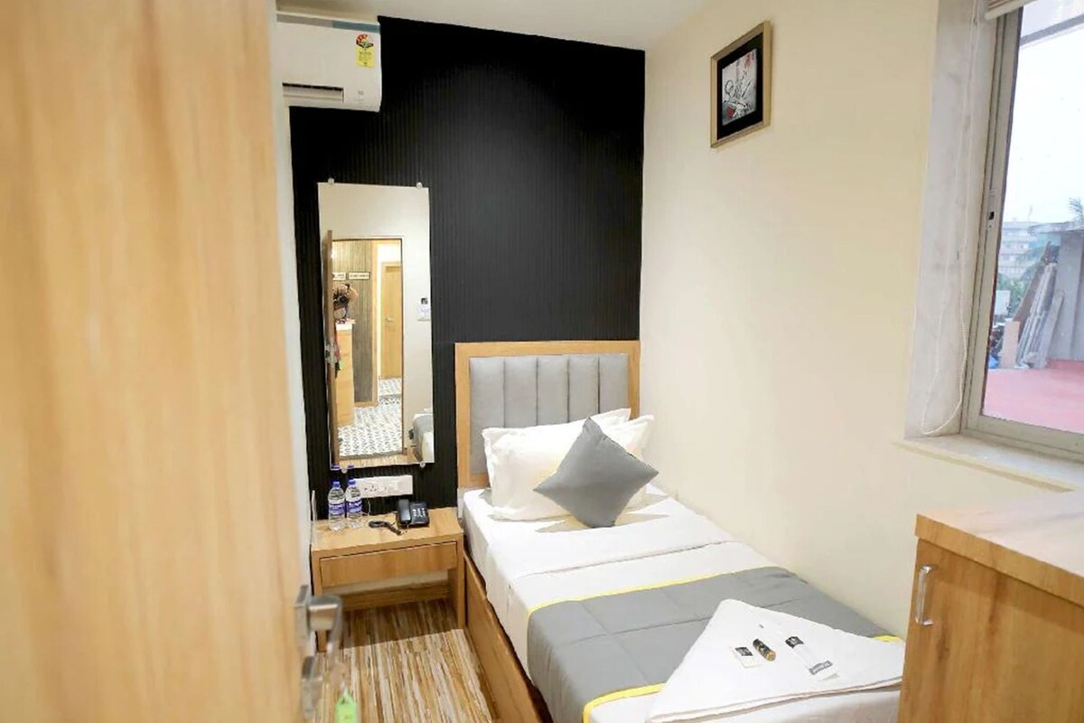 A hotel room with a bed, bedside table, mirror, ceiling fan, and a window.