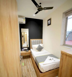 A hotel room with a bed, bedside table, mirror, ceiling fan, and a window. - Cabinstay Airport (Mumbai)
