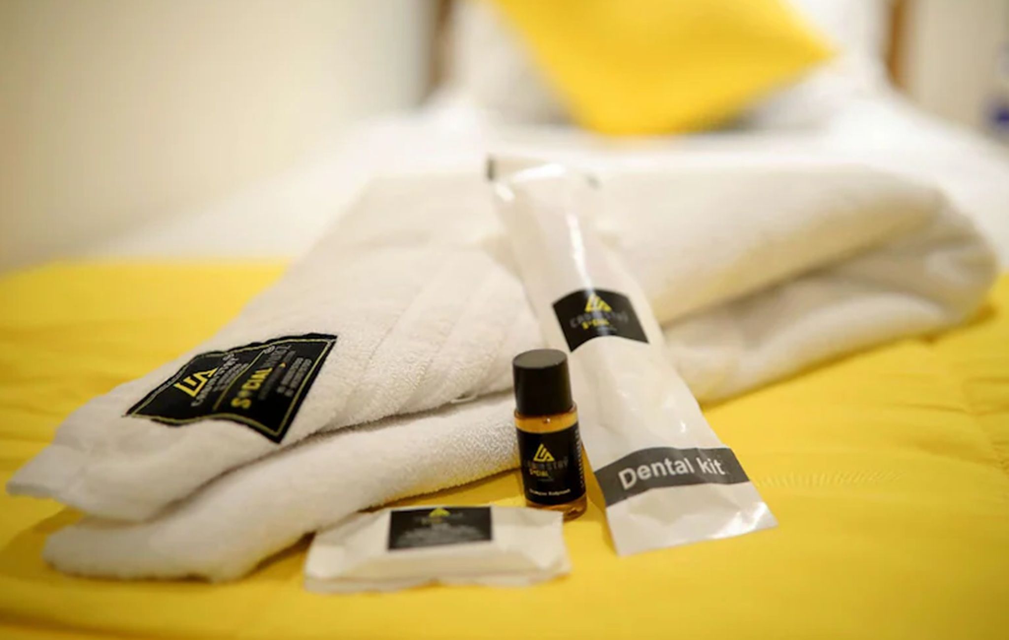 A bed with a yellow bedspread, a white towel, and a dental kit on it.