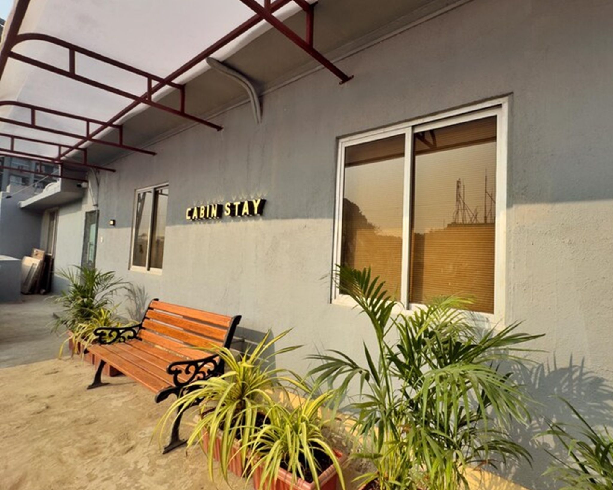Un edificio con un letrero que dice 'CABIN STAY' y un banco de madera con plantas en macetas al frente.