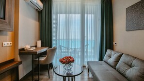 Une chambre d’hôtel moderne dotée d’un coin repas, d’un canapé et d’un balcon avec des rideaux légers.