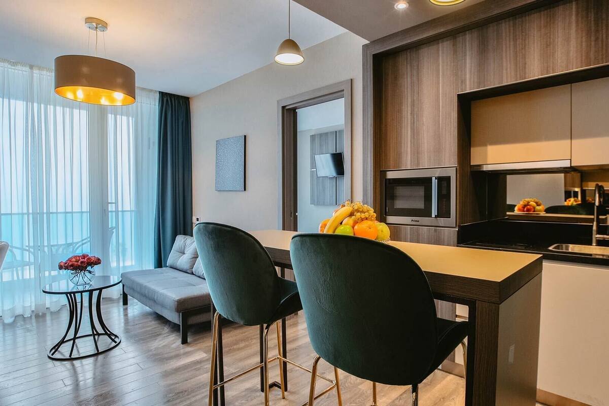 A modern apartment with a dining area, a sofa, a TV, and a kitchen with a microwave.