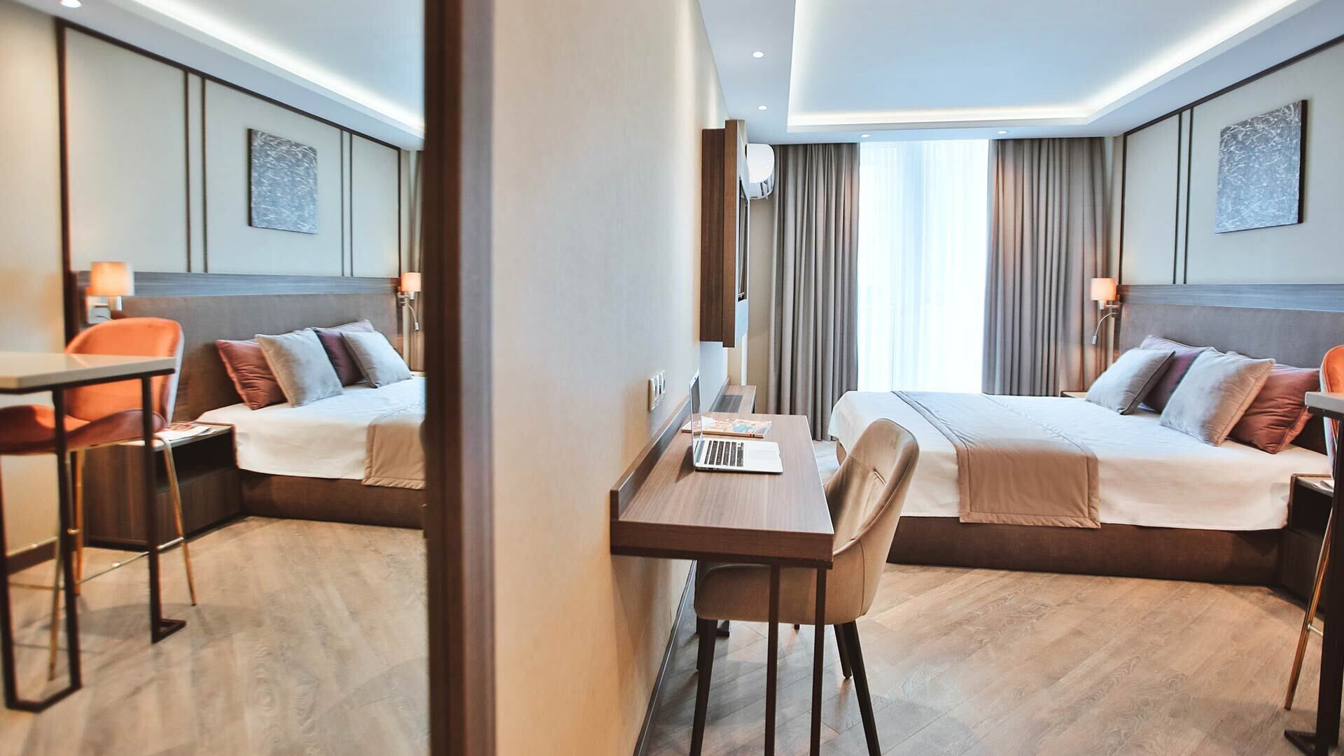 Hotellihuoneessa on kaksi sänkyä, työpöytä ja tuoli. Työpöydällä on kannettava tietokone, ja huoneen sisustus on moderni ja värit ovat hillittyjä.