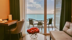 A hotel room with a balcony, a dining table with chairs, a sofa, and a vase of red roses.