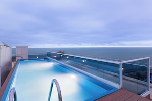 Une piscine dotĂ©e de rampes en verre, dâune terrasse en bois et offrant une vue sur la mer.
