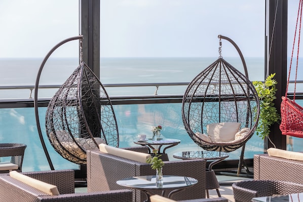 A balcony with wicker furniture, a small table with a vase, and a view of the ocean.