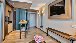 Ein modernes Hotelzimmer mit Holzboden, einer Essecke mit Tisch und Stühlen, einem an der Wand montierten Fernseher und einer Sitzbank.