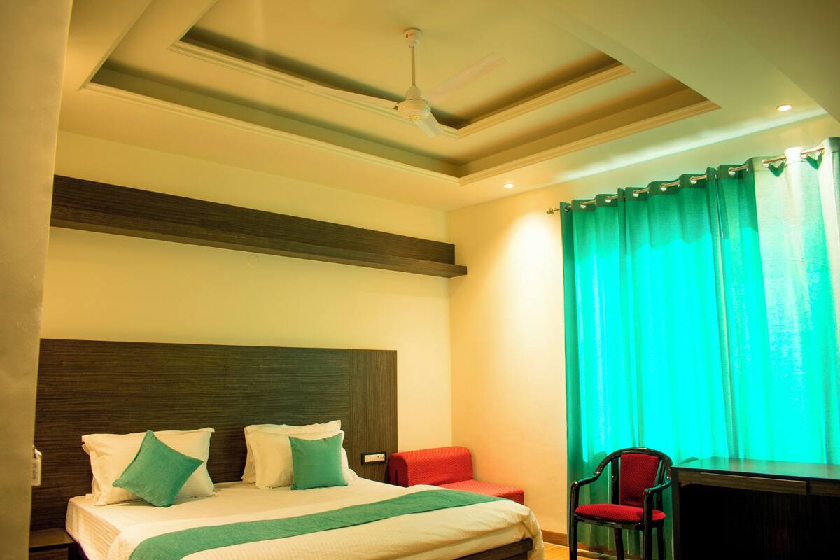 A hotel room with a bed, a desk, a chair, a ceiling fan, and a window with curtains.