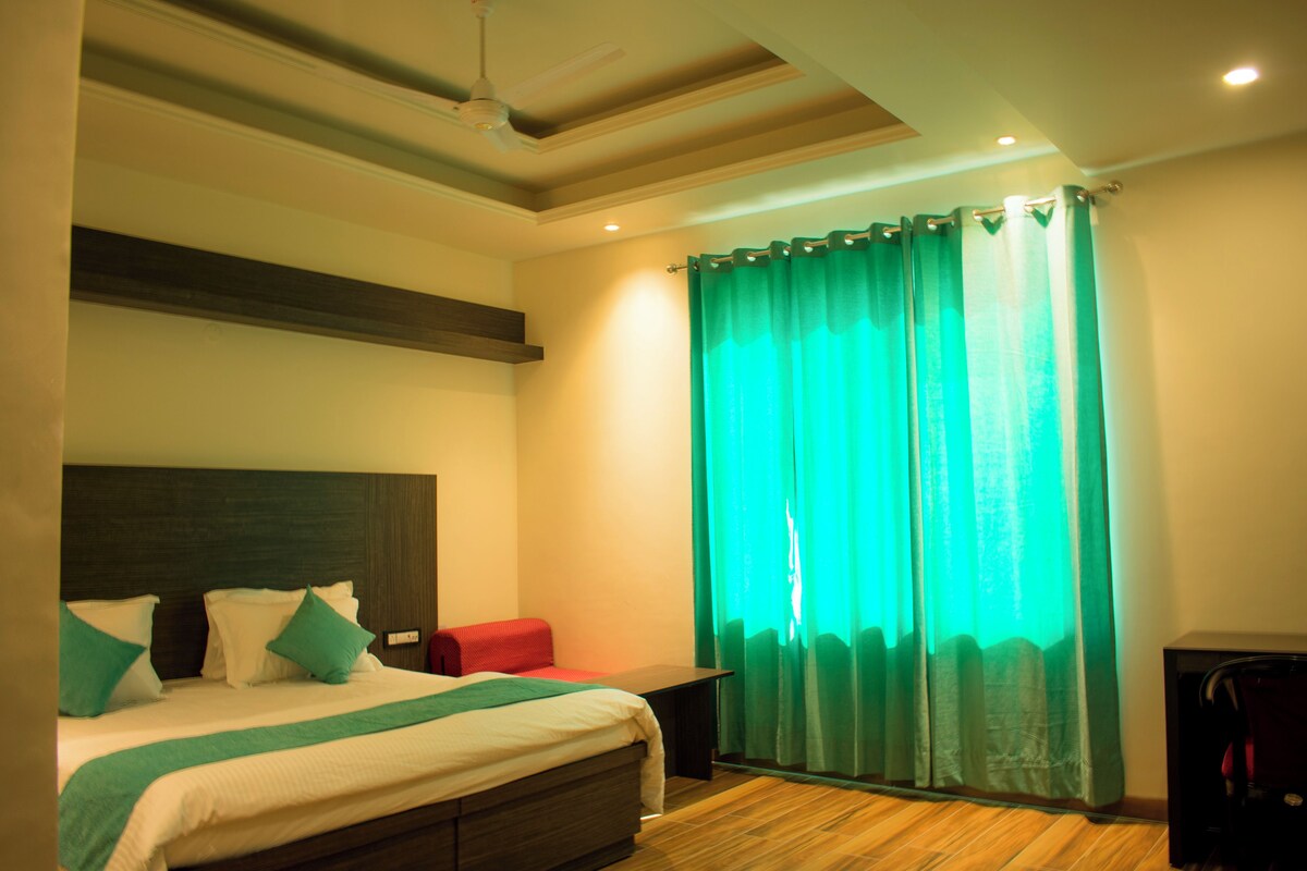 A hotel room with a bed, a desk, a chair, a window with curtains, and a ceiling fan.