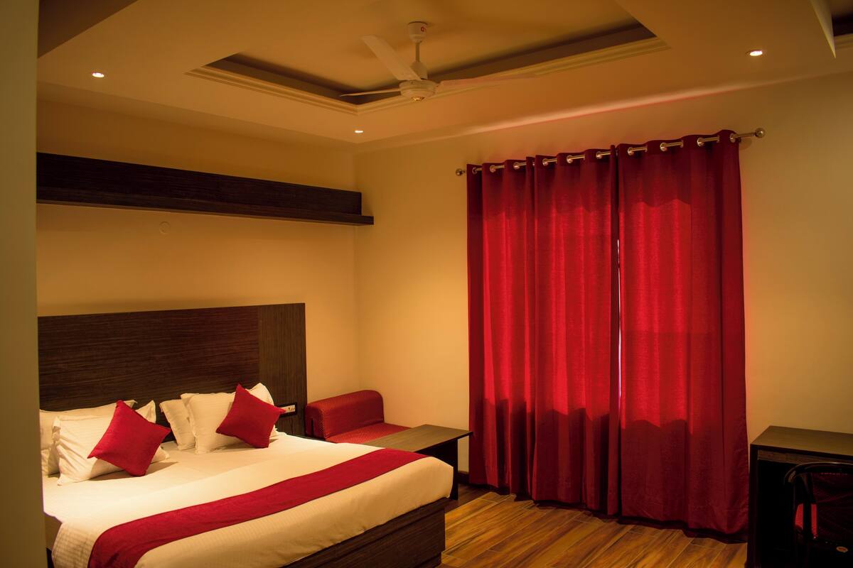 A hotel room with a bed, a nightstand, a red curtain, and a ceiling fan.