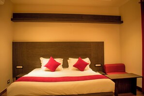A hotel room with a large bed, a wooden headboard, a red chair, and a small table. - Hotel Chancellor (Jalandhar)