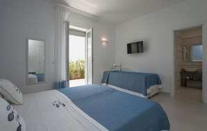 Ein Schlafzimmer mit Bett, Fernseher, Badezimmer und einem Fenster mit Vorhängen.