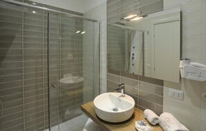 Ein modernes Badezimmer mit einer Duschkabine, einem runden Waschbecken mit Spiegel darüber und einem Handtuchhalter.