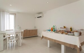Ein helles, weißes Zimmer mit Frühstückstisch, Küchenzeile und Klimaanlage.
