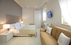 Ein Hotelzimmer mit Bett, Nachttisch, Fernseher und einer Couch.