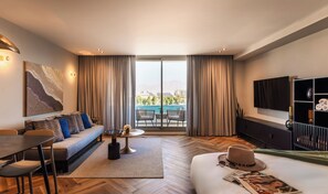A modern hotel room with a sofa, dining table, chairs, a TV, and a balcony with a view. - Sphera Eilat Hotel (Eilat)