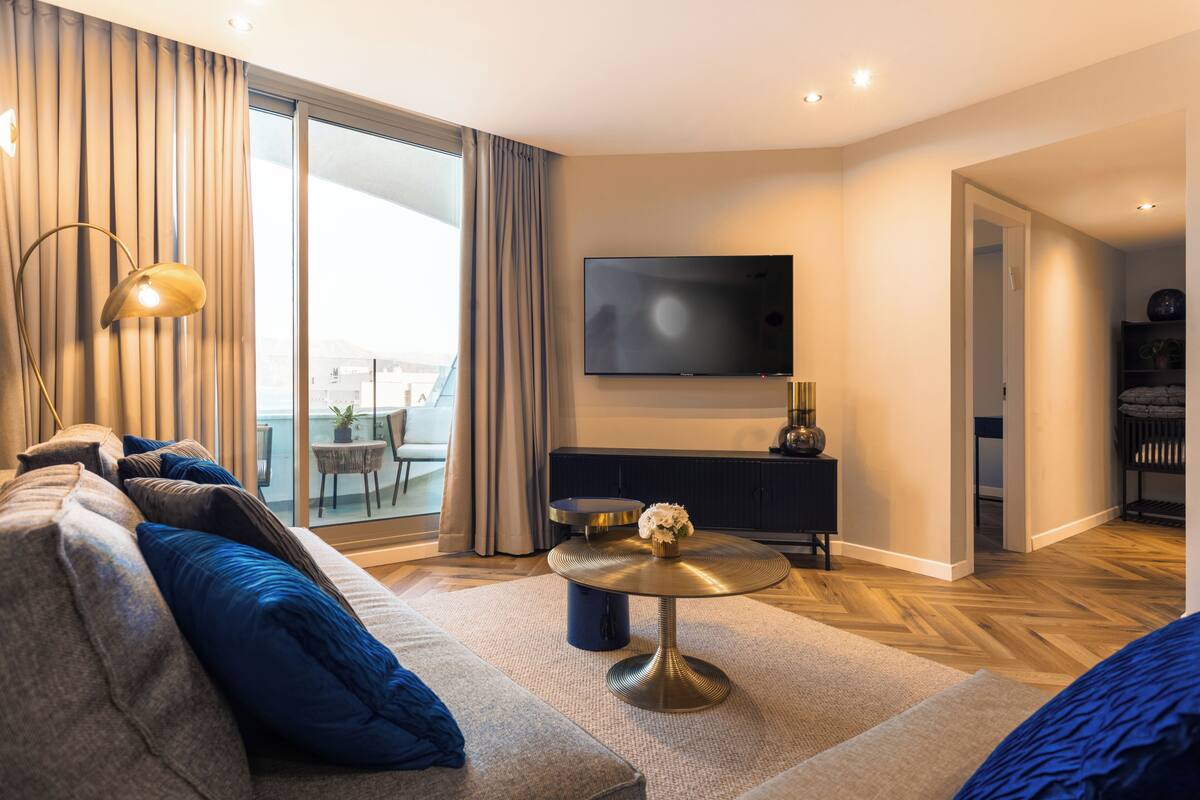 A modern living room with a sofa, a round coffee table, a flat-screen TV, and a view of the outdoors.