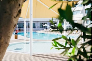 A pool area with lounge chairs and umbrellas, surrounded by a building with large windows.
