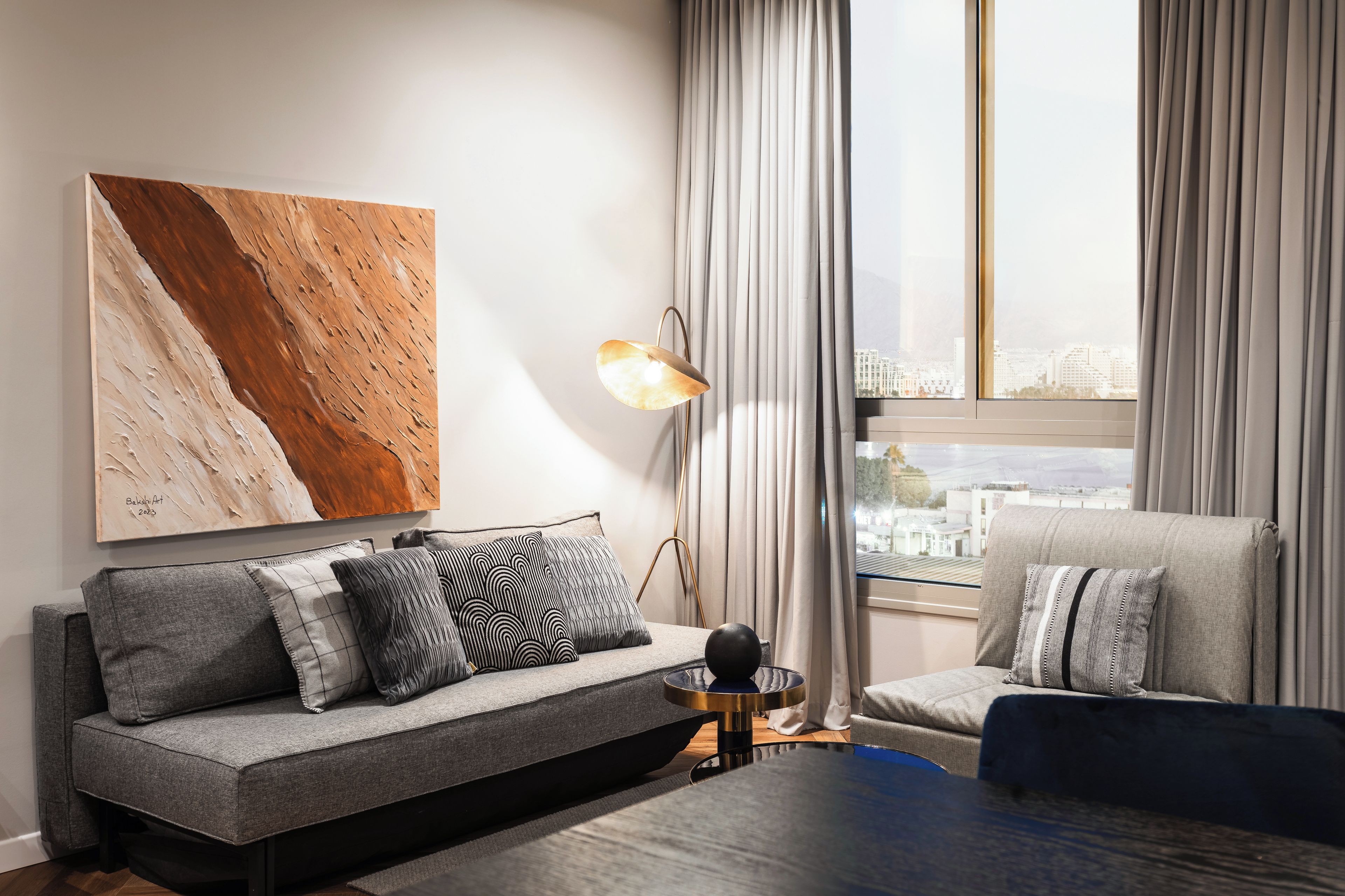 A modern living room with a sofa, armchair, and a large abstract painting on the wall.