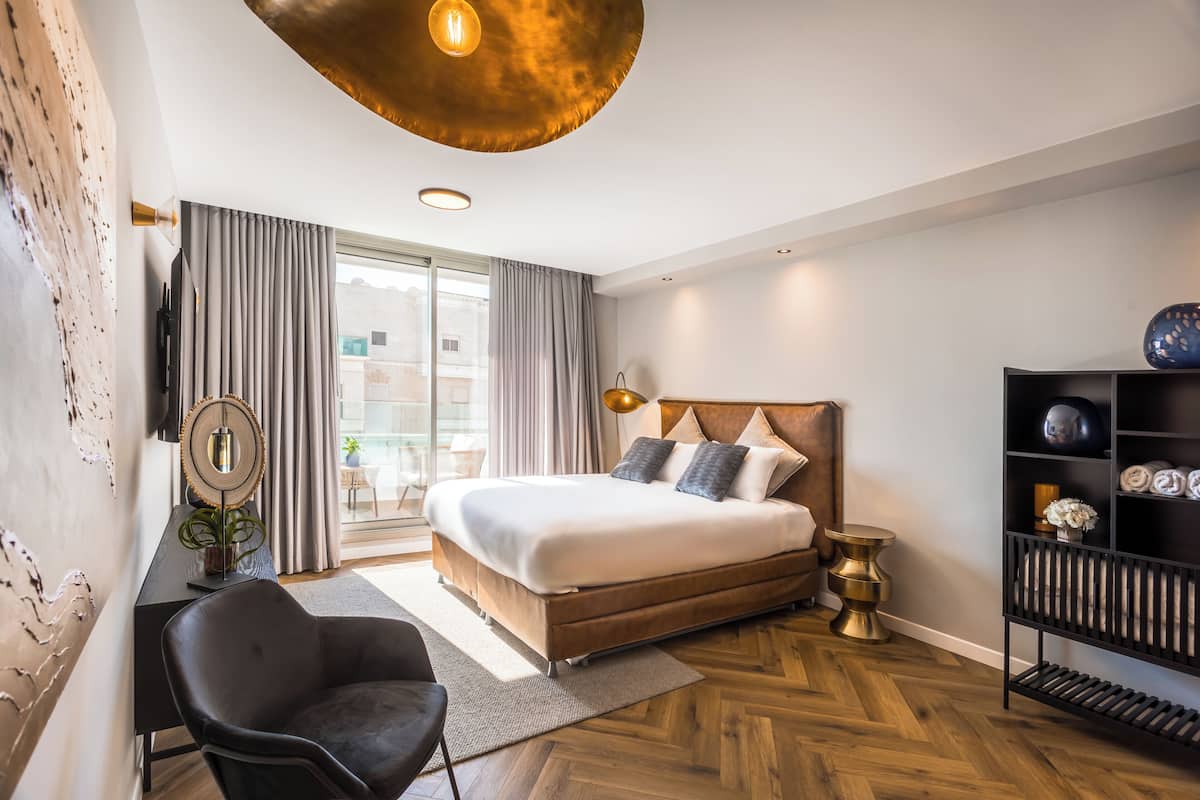 A modern bedroom with a large bed, a desk, a chair, a bookshelf, and a view of the outside.