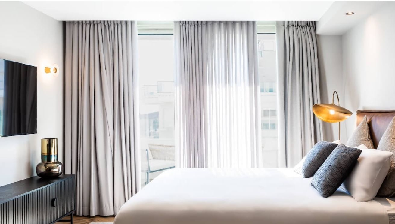 A modern hotel room with a large bed, a flat-screen TV, a desk, and a view of the city.