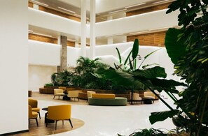 A spacious lobby with multiple seating areas, a central plant arrangement, and a modern architectural design. - Sphera Eilat Hotel (Eilat)