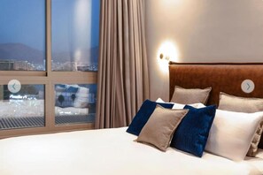 A hotel room with a large bed, a view of the city through a window, and a night sky visible through the curtains. - Sphera Eilat Hotel (Eilat)