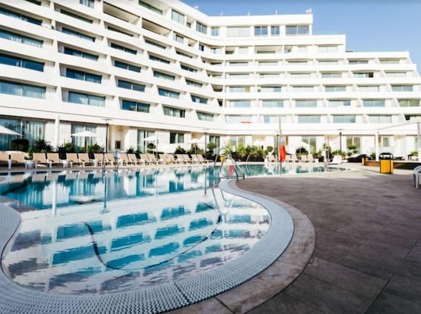 Un hotel moderno con una piscina grande, varios balcones y un cielo despejado.