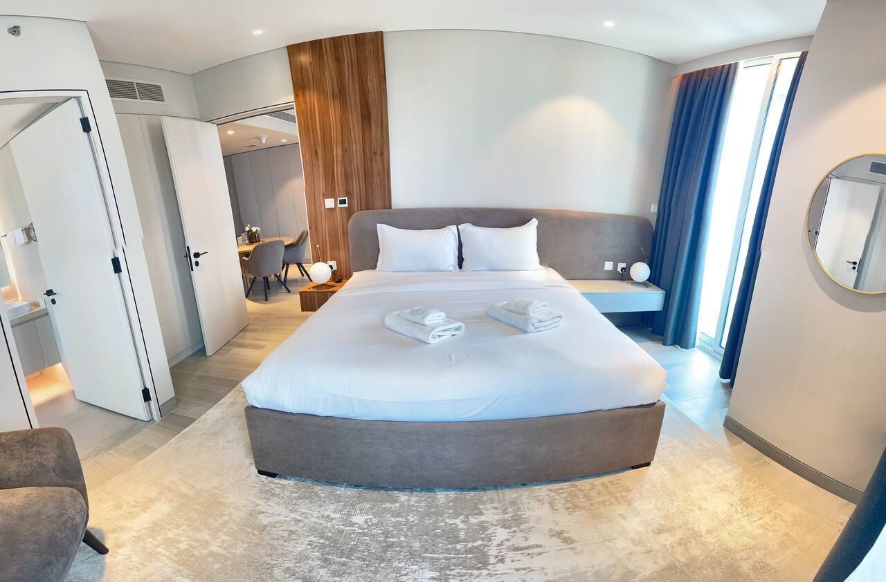 Een moderne hotelkamer met een groot bed, een zithoek, een eettafel en een badkamer die door een open deur zichtbaar is.