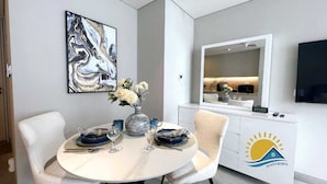 A modern dining area with a round table, white chairs, a vase with flowers, and a white cabinet with a logo. - Dubai Marina Walk Gem (Dubai)