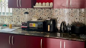 Uma cozinha com micro-ondas, torradeira, cafeteira e uma estante com pratos e copos.
