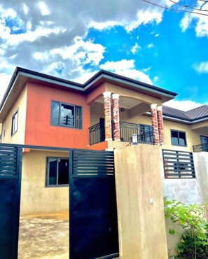 A two-story house with a balcony, a gated entrance, and a clear sky. - Serene Hostel Accra (Adenta Municipality)