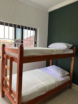 A bunk bed with white bedding, a window with bars, and a green wall. - Serene Hostel Accra (Adenta Municipality)