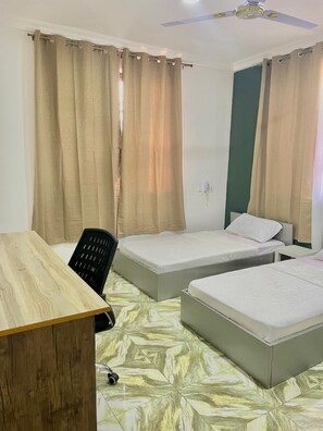 A room with two beds, a desk, a chair, and a ceiling fan. - Serene Hostel Accra (Adenta Municipality)