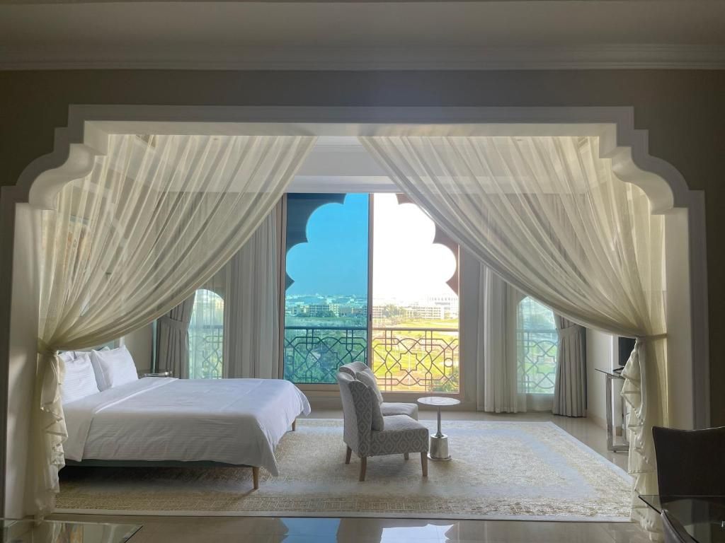 A bedroom with a bed, a chair, a small table, and a view of a balcony.