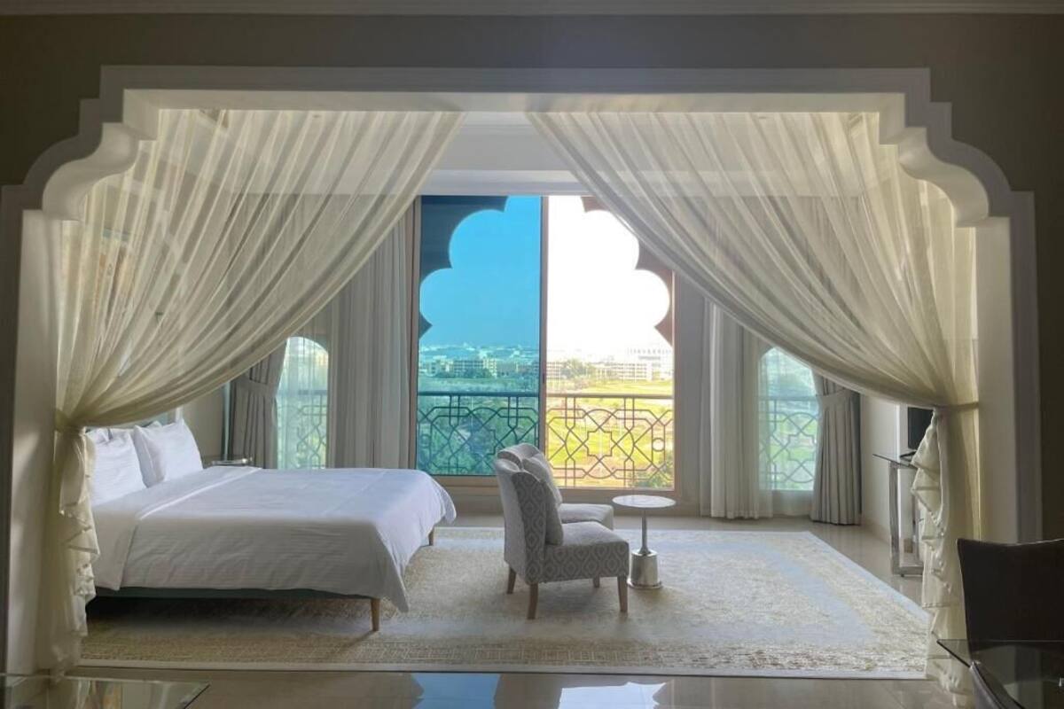 A bedroom with a bed, a chair, a small table, and a view of a balcony.