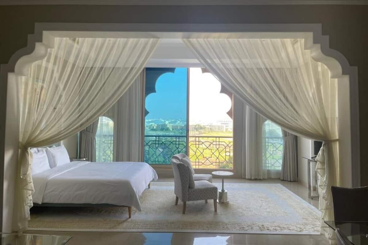 A bedroom with a bed, a chair, a small table, and a view of a balcony.