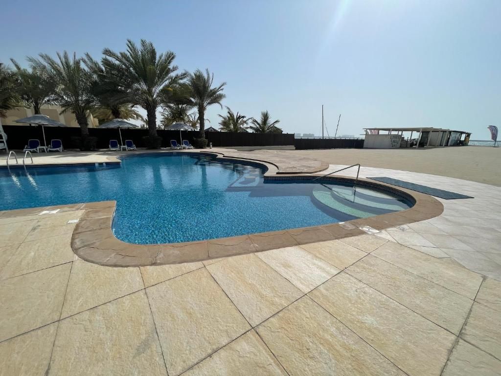 A swimming pool with a curved edge, surrounded by palm trees and lounge chairs.
