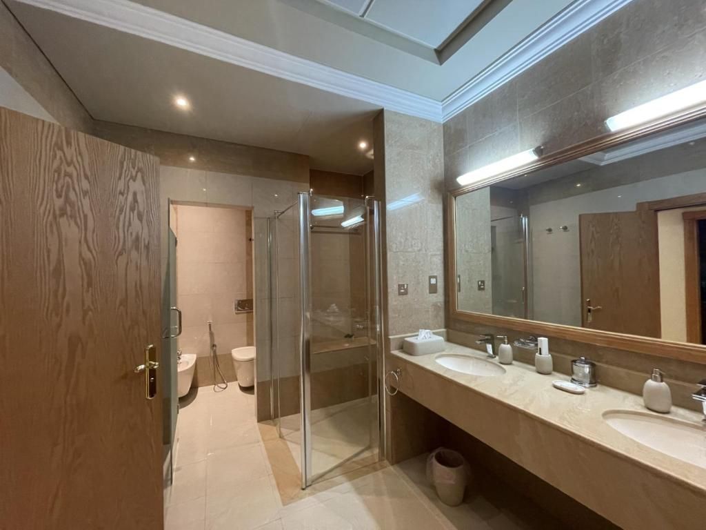 Un baño moderno con cabina de ducha de vidrio, tocador doble y un espejo grande.