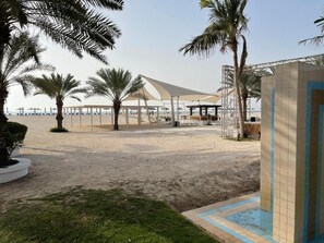 Zona de playa con palmeras, un área de estar cubierta y una piscina.