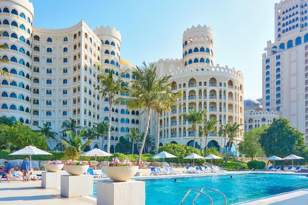 A hotel with a large pool, palm trees, and a white facade with blue accents.