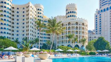 A hotel with a large pool, palm trees, and a white facade with blue accents.