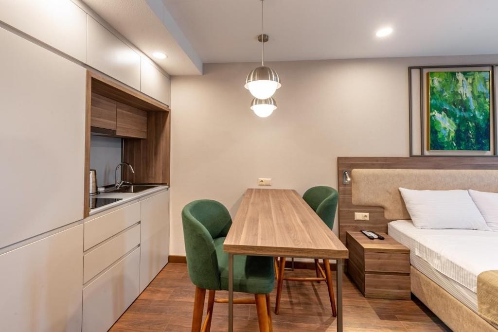 A compact room with a kitchenette, a dining table with chairs, a bed, and a painting on the wall.