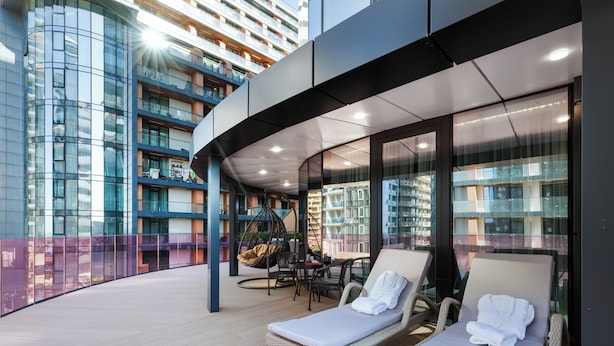 A modern indoor balcony with lounge chairs, a hanging chair, and a glass wall offering views of a high-rise building. - Rainbow Residence (Batumi)