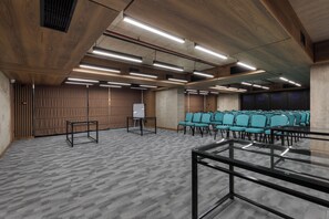 Ein Konferenzraum mit Teppichboden, Holzwandverkleidung und Reihen von türkisfarbenen Stühlen.